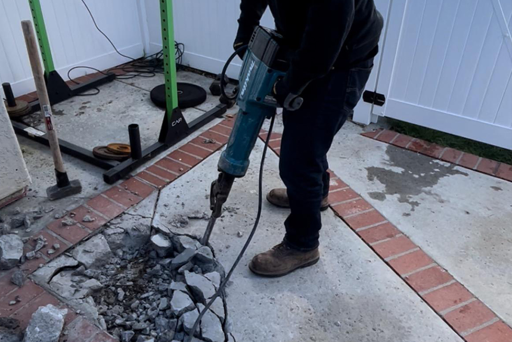 worker using concrete cutting equipment on damaged floor surface with brick border
